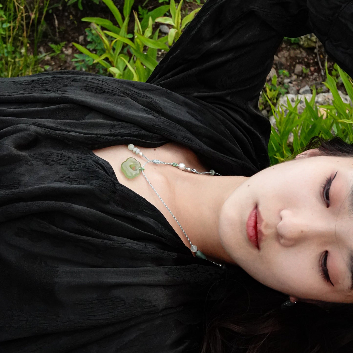 Person lying on grass wearing a black dress and green jade necklace