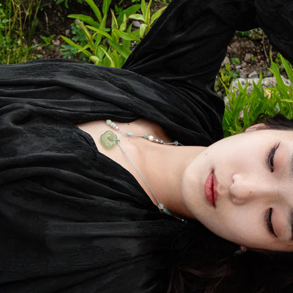Person lying on grass wearing a black dress and green jade necklace